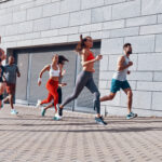 Full length of young people in sports clothing jogging while exercising on the sidewalk outdoors